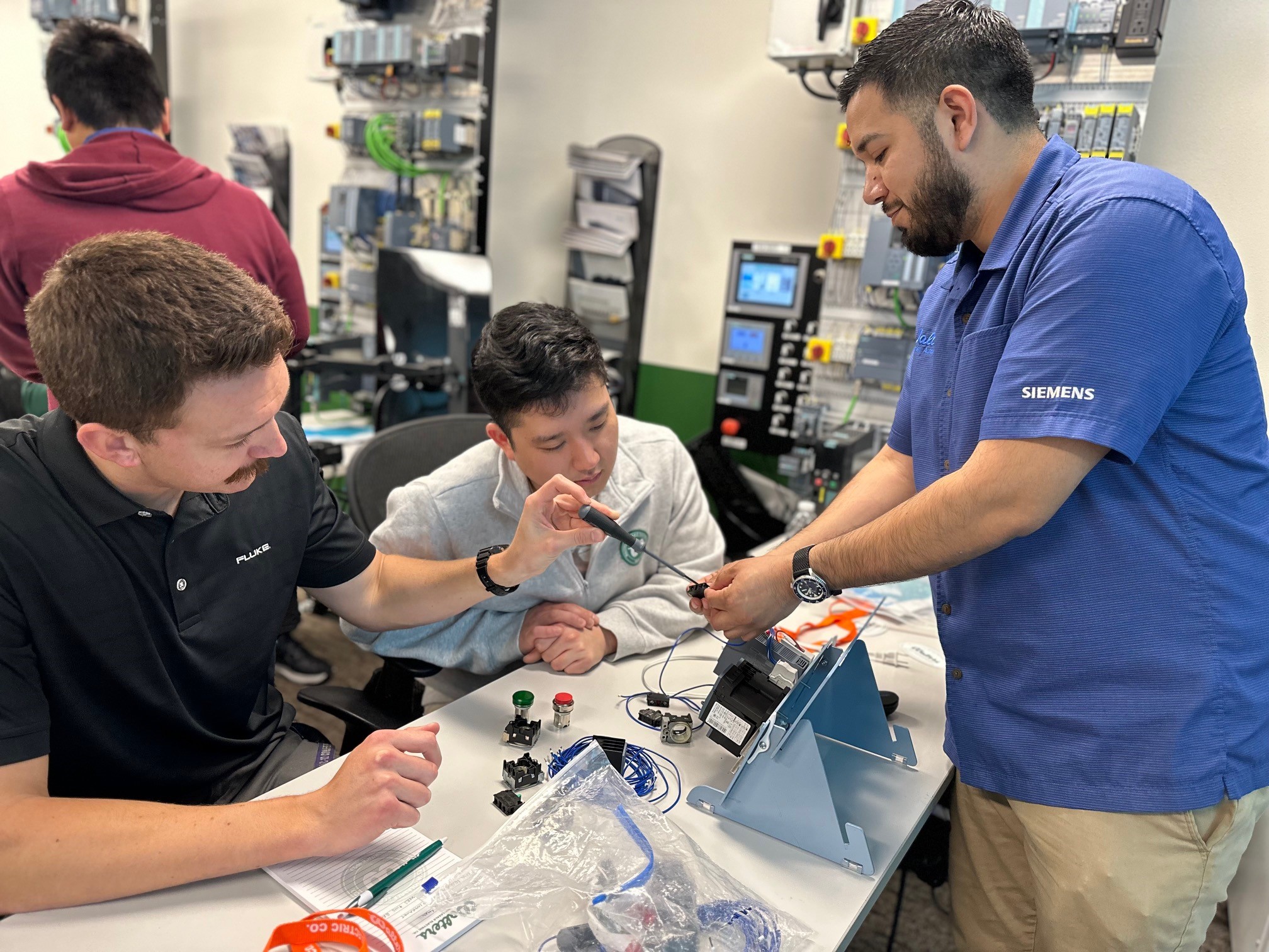 Hands-on industrial controls and automation training with electrical technicians wiring control components and PLC systems.