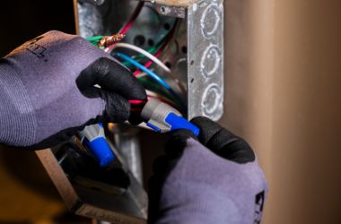 Electrician securing wire connections with twist-on wire connectors inside a metal junction box.
