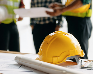 Contractor consultation outside residential jobsite with hard hat and plans—supporting electrical project planning and service questions.
